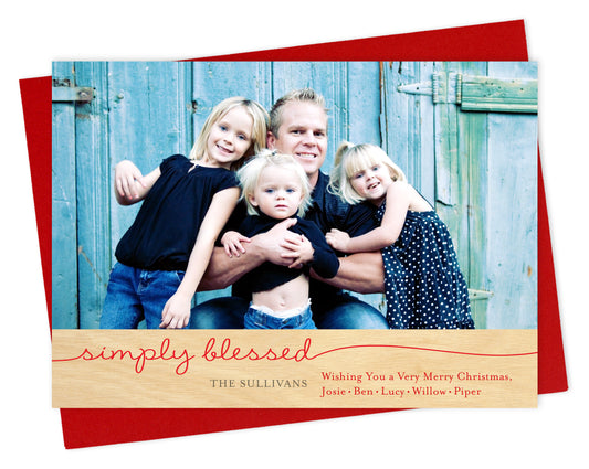 Customizable paper holiday card featuring a family photo and a printed birch wood grain border at the bottom that reads "simply blessed" along with a personal greeting. Shown with a red envelope.