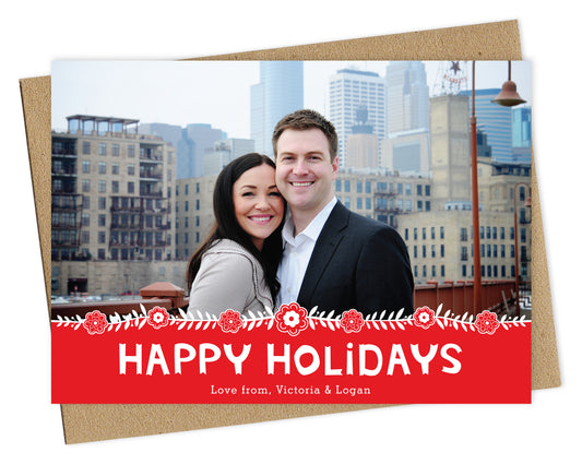 Customizable paper holiday card featuring a photo across the top, Scandinavian-inspired florals, and a red banner that reads “Happy Holidays.” Shown with a kraft envelope.