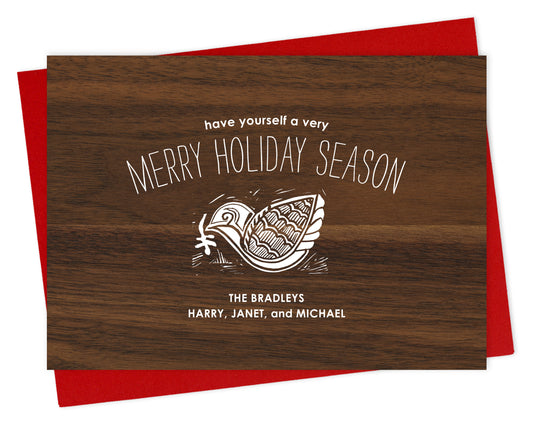 Customizable paper holiday card with a knock-out style dove, “Have Yourself a Merry Holiday Season” text and a personal message on a printed walnut wood grain background. Shown with a red envelope.