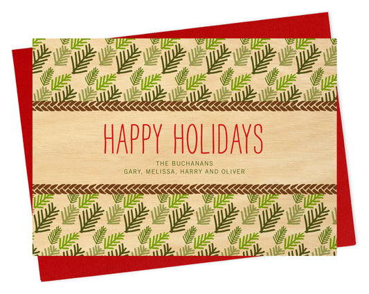 Front of personalized paper holiday card with evergreen leaf pattern, "Happy Holidays" text and a personal greeting on a printed birch wood background. Shown with a red envelope.