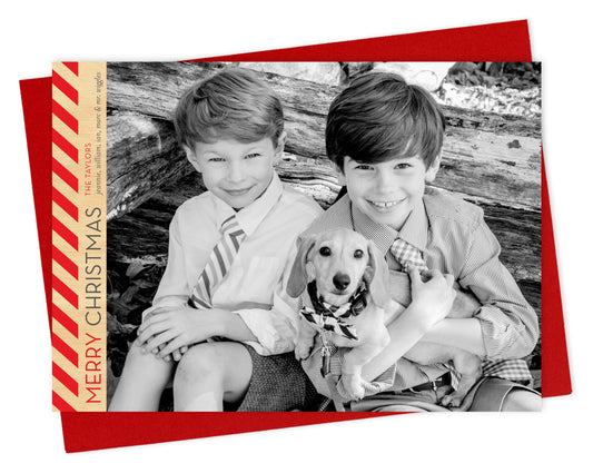 Customizable paper holiday card featuring a landscape photo with bold diagonal red stripes, “MERRY CHRISTMAS” text and a personal greeting running vertically along the left side. Shown with a red envelope.