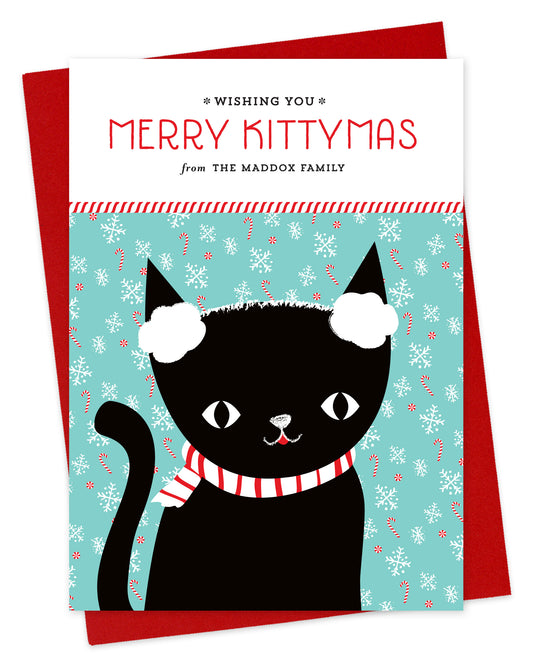 Customizable paper holiday card featuring a black cat wearing earmuffs in front of a festive backdrop, a "Merry Kittymas" sentiment and a personal greeting. Shown with a red envelope.