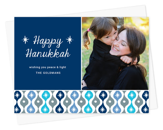 Customizable paper Hanukkah photo card featuring a family picture and personal message on a blue background with a decorative sparkle design banner in shades of blue. Shown with white envelope.