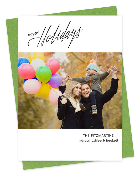 Customizable paper holiday card featuring your photo bordered by white with black "Happy Holidays" text near the top and your personal greeting at the bottom. Shown with a green envelope.