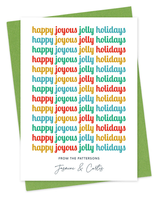 Customizable paper holiday card featuring cheerful, multicolored “Happy Joyous Jolly Holidays” text repeated down the length of the card and a personal greeting at the bottom. Background of card is white. Shown with a green envelope.