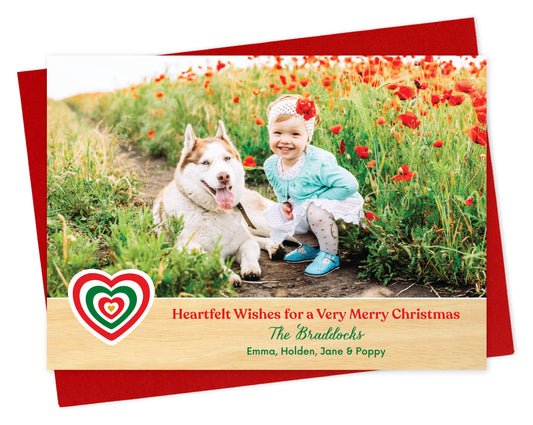Customizable paper holiday card featuring a photo above a printed birch wood grain border. The border includes a red and green heart, 'Heartfelt Wishes for a Very Merry Christmas' text and a personal greeting. Card shown on a red envelope.