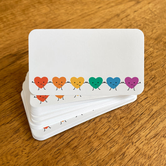 A stack of small white Happy Hearts mini note cards with rounded corners, featuring a row of smiling rainbow heart characters holding hands.