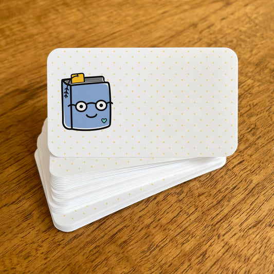 A stack of small white Book Lover note cards with rounded corners, featuring a cute, smiling blue book wearing glasses and a pale yellow dotted background.