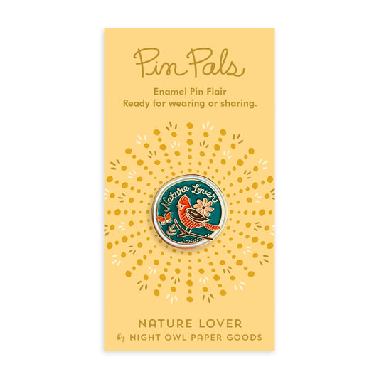 Nature Lover enamel pin on a yellow backer card. Pin features a blue background with a red and brown bird, a peach flower, a butterfly and the words 'Nature Lover' in gold script. Backer card reads "Pin Pals Enamel Pin Flair Ready for wearing or sharing. NATURE LOVER by Night Owl Paper Goods.