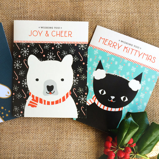 Two Christmas cards featuring a polar bear wearing a scarf with text 'Wishing you Joy & Cheer' and a black cat wearing earmuffs with text 'Wishing you Merry Kittymas'.