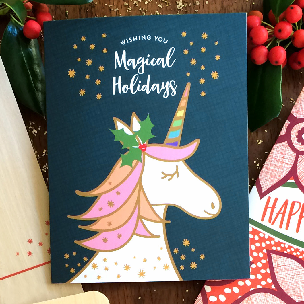 Unicorn-themed holiday card with dark blue background and "Wishing you Magical Holidays" text, surrounded by festive decorations