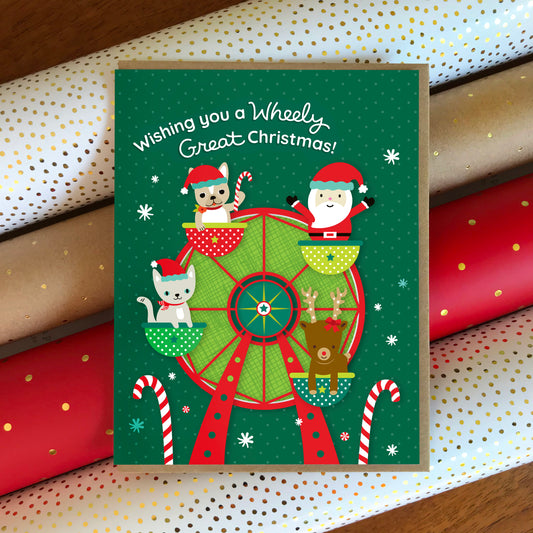 Christmas card with Santa, reindeer, and dog and cat on a Ferris wheel with wrapping paper in the background. Text reads 'Wishing you a wheely great Christmas!'