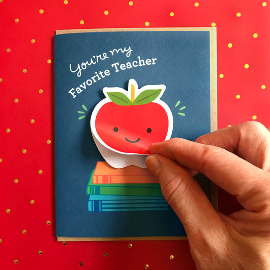Teacher card featuring an apple on a stack of illustrated books and a hand and fingers showing how the vinyl sticker is easy for recipient to remove and use.
