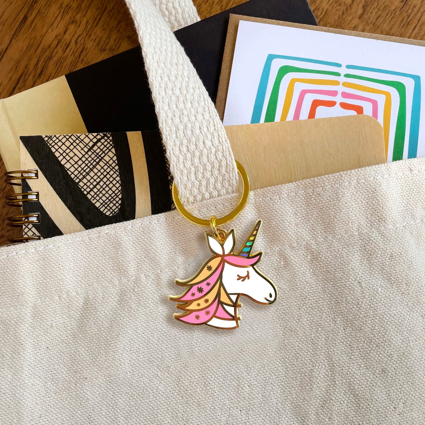 Unicorn enamel keychain hanging from a tote bag handle