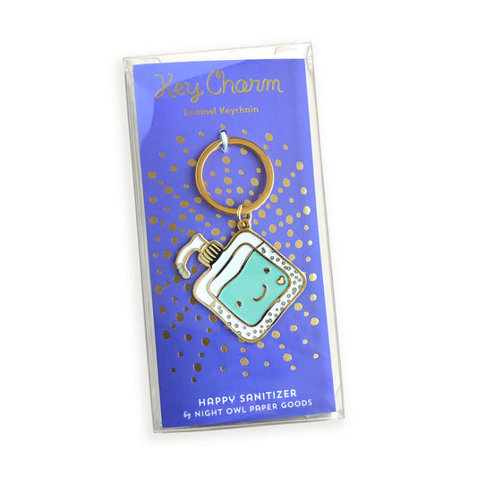 Hand sanitizer enamel keychain on gold foil stamped backer card packaged in a clear gift box. Backer card reads "Key Charm Enamel Keychain" at top and "Happy Sanitizer by Night Owl Paper Goods" at bottom.