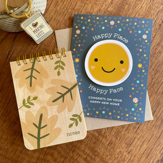 Group of products including Modern Leaves wood mini notepad, Happy Place New Home Sticker greeting card and Making Lists keychain.