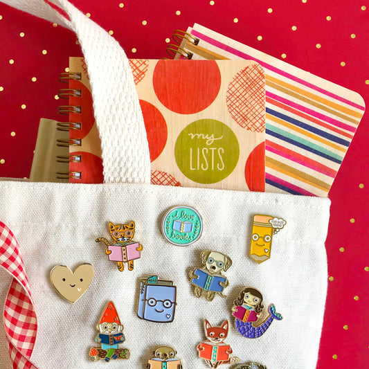 Collection of colorful notebooks and pins on a white tote bag with a red background