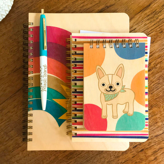 Dotty Doggie wood mini notepad and a notebook with colorful rainbow design displayed with a teal Magic Wand pen on a wood surface.