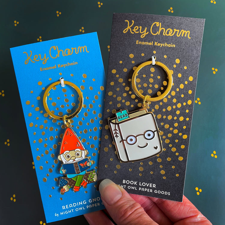 Gnome and Book Lover keychains displayed on gold foil-stamped backer cards