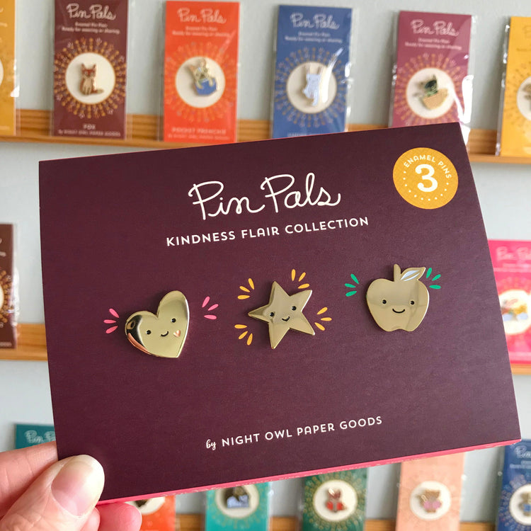 Three shiny gold enamel pins on packaging. Heart to show love. Star to reward achievement. Apple to inspire healthy choices.