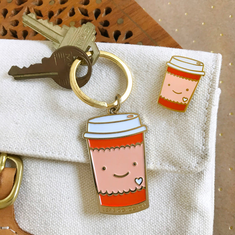 Travel coffee cup with smile face and matching enamel pin. Both are orange and peach.