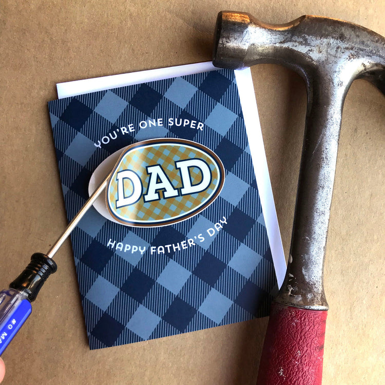 Blue plaid Father's Day Dad card with oval shape removable vinyl sticker that has a manly gingham pattern and read 'Dad'.'