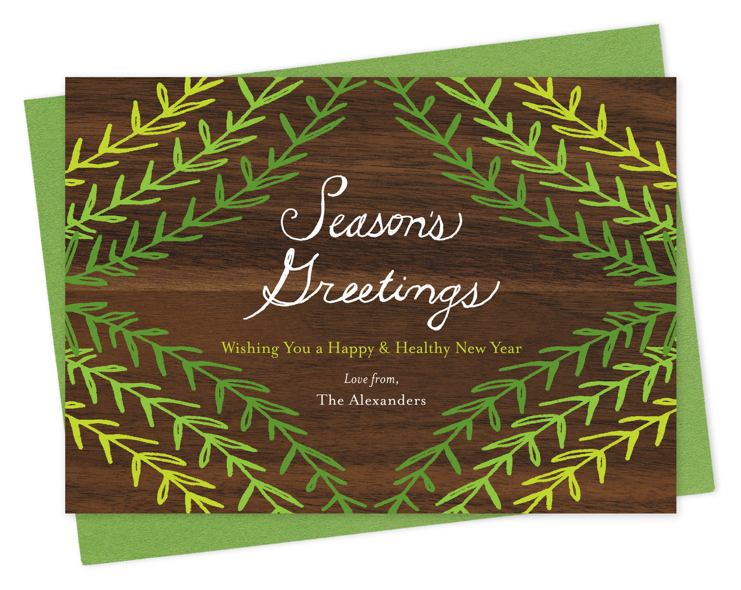 Customizable paper holiday card with green sprig design, "Season's Greetings" sentiment and a personal message on a printed walnut wood grain background. Shown with a green envelope.