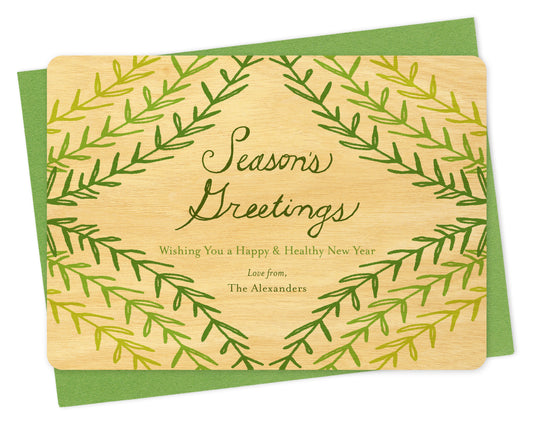 Customizable wood holiday card with green sprig design, "Season's Greetings" sentiment and a personal message on a birch wood card. Shown with a green envelope.