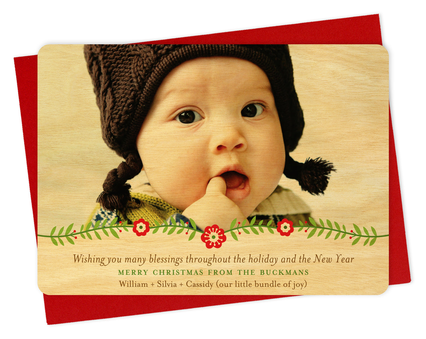 Customizable wood holiday card featuring a photo with a floral garland and birch wood grain border at the bottom and a personal greeting. Shown with a red envelope.