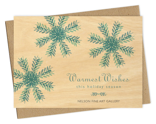 Customizable paper holiday card featuring blue snowflakes on a printed birch wood background with space for a logo and/or personal message. Shown with a kraft envelope.