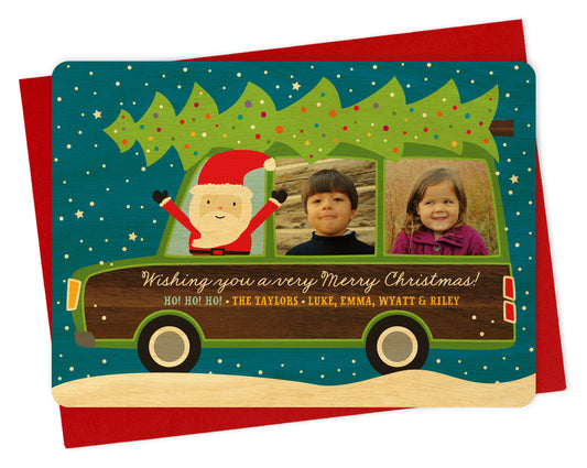 Customizable wood holiday card featuring your family photos in the windows of a wood-paneled station wagon with Santa driving and a personal greeting on the side of the car. Shown with a red envelope.