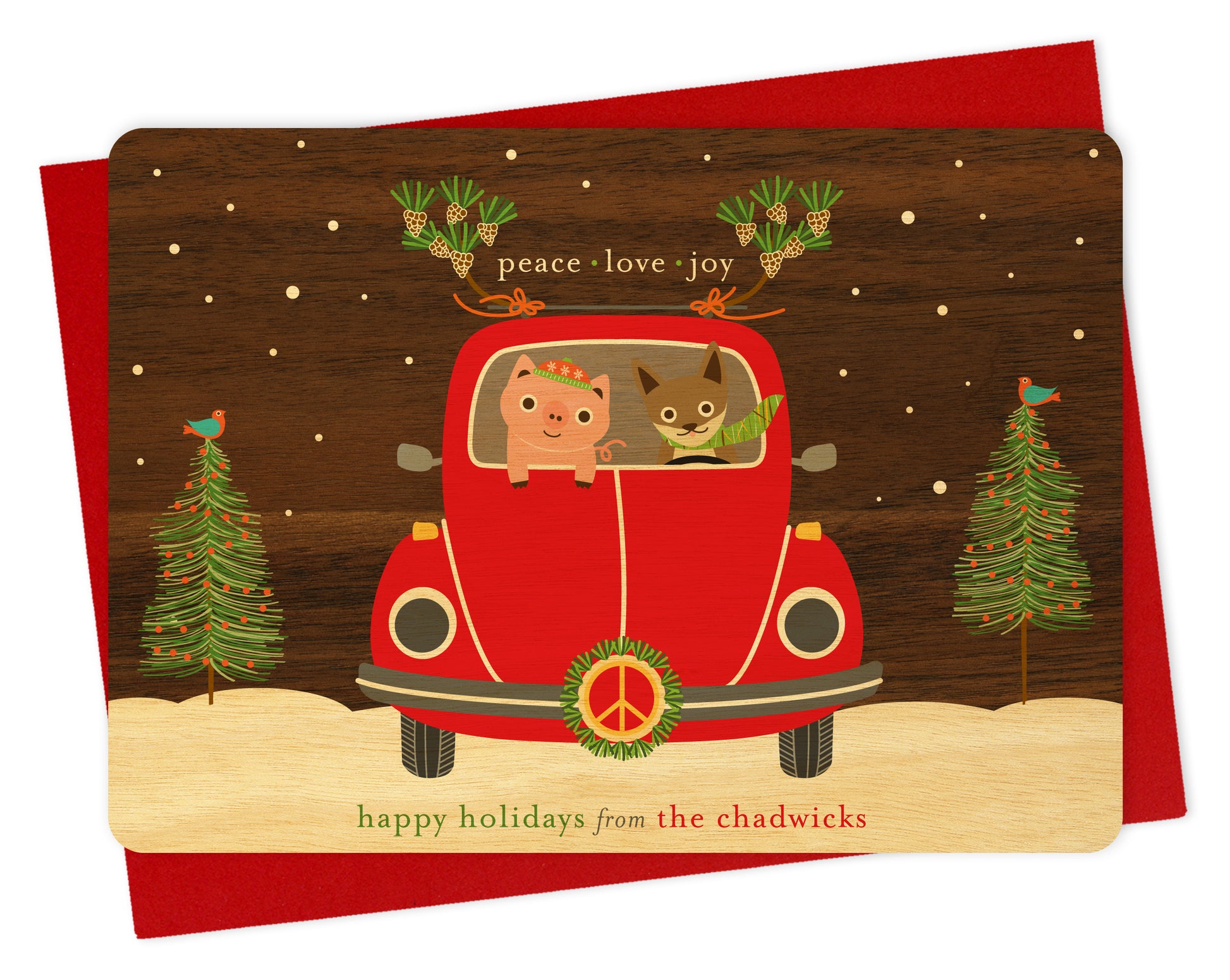 Customizable birch wood holiday card with fun illustration of a pig and fox riding in a red car with peace symbol and wreath on the front of the car with a printed walnut wood grain sky. Card features “Peace Love Joy” sentiment and a personal greeting. Shown with a red envelope.