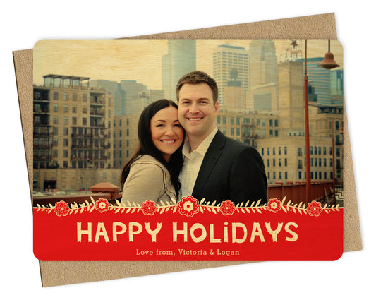 Customizable wood holiday card featuring a photo across the top, Scandinavian-inspired florals, and a red banner that reads “Happy Holidays.” Shown with a kraft envelope.