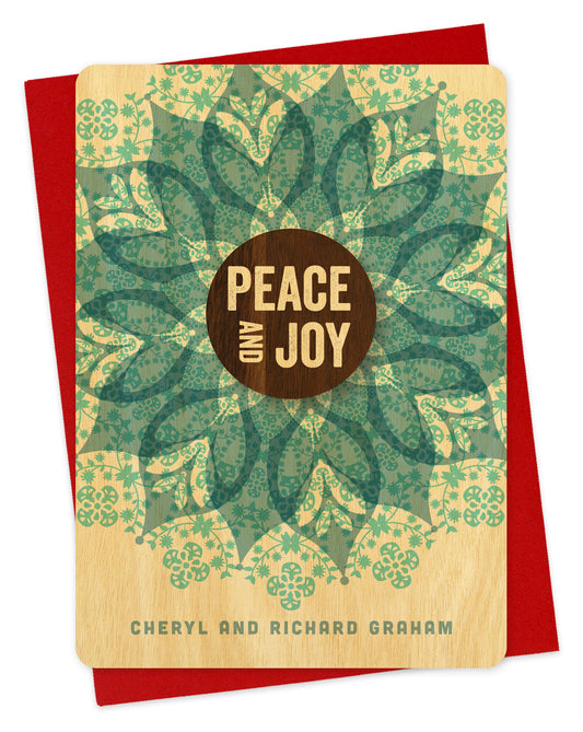 Customizable wood holiday card featuring a detailed blue blossom with a walnut wood grain medallion in the middle that reds “Peace and Joy.” Personal text is at the bottom. Shown with a red envelope.