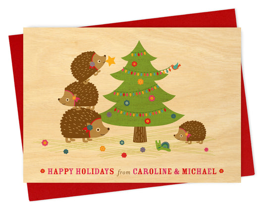 Customizable birch wood Christmas card with hedgehogs and a decorated tree, "Happy Holidays" text and personal message on a printed birch wood background. Show with a red envelope. 