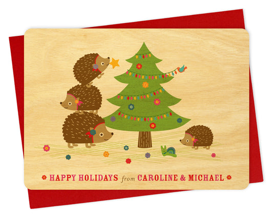 Customizable birch wood Christmas card with hedgehogs and a decorated tree, "Happy Holidays" text and personal message. Show with a red envelope. 