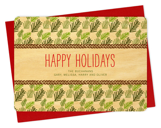 Front of personalized wood holiday card with evergreen leaf pattern, "Happy Holidays" text and a personal greeting on a natural birch wood background. Shown with a red envelope.