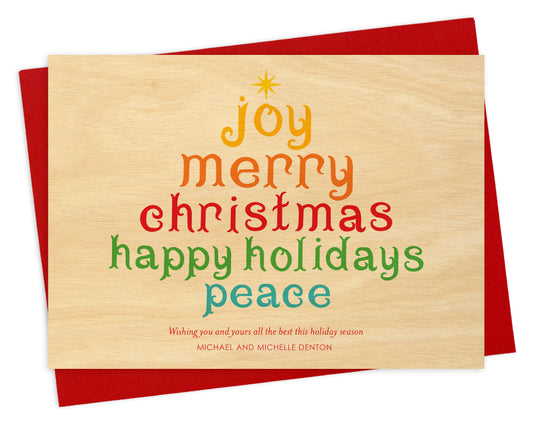 Front of personalized wood holiday card  featuring a colorful tree formed from festive “Joy, Merry Christmas, Happy Holidays, Peace” text on a printed birch wood grain background. Shown with red envelope.
