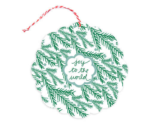 Front of customizable paper holiday ornament card with festive evergreen sprigs and "Joy to the World" text on a white background. Round ornament with scalloped edges.