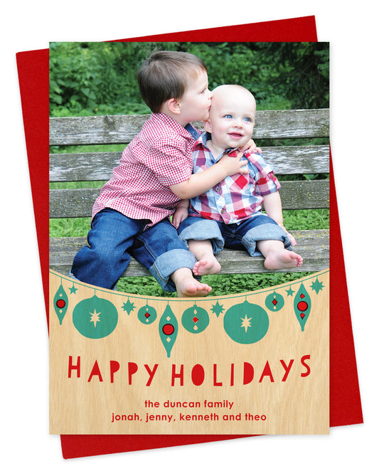 Customizable paper holiday card featuring your photo, festive aqua and red hanging ornaments, 'Happy Holidays' text and a personal greeting on a printed birch wood grain background. Shown on a red envelope.