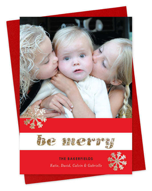 Customizable paper holiday card featuring a photo across the top, a red and white striped banner with snowflakes and “Be Merry” in glittery gold font, plus a personal greeting. Shown with a red envelope.