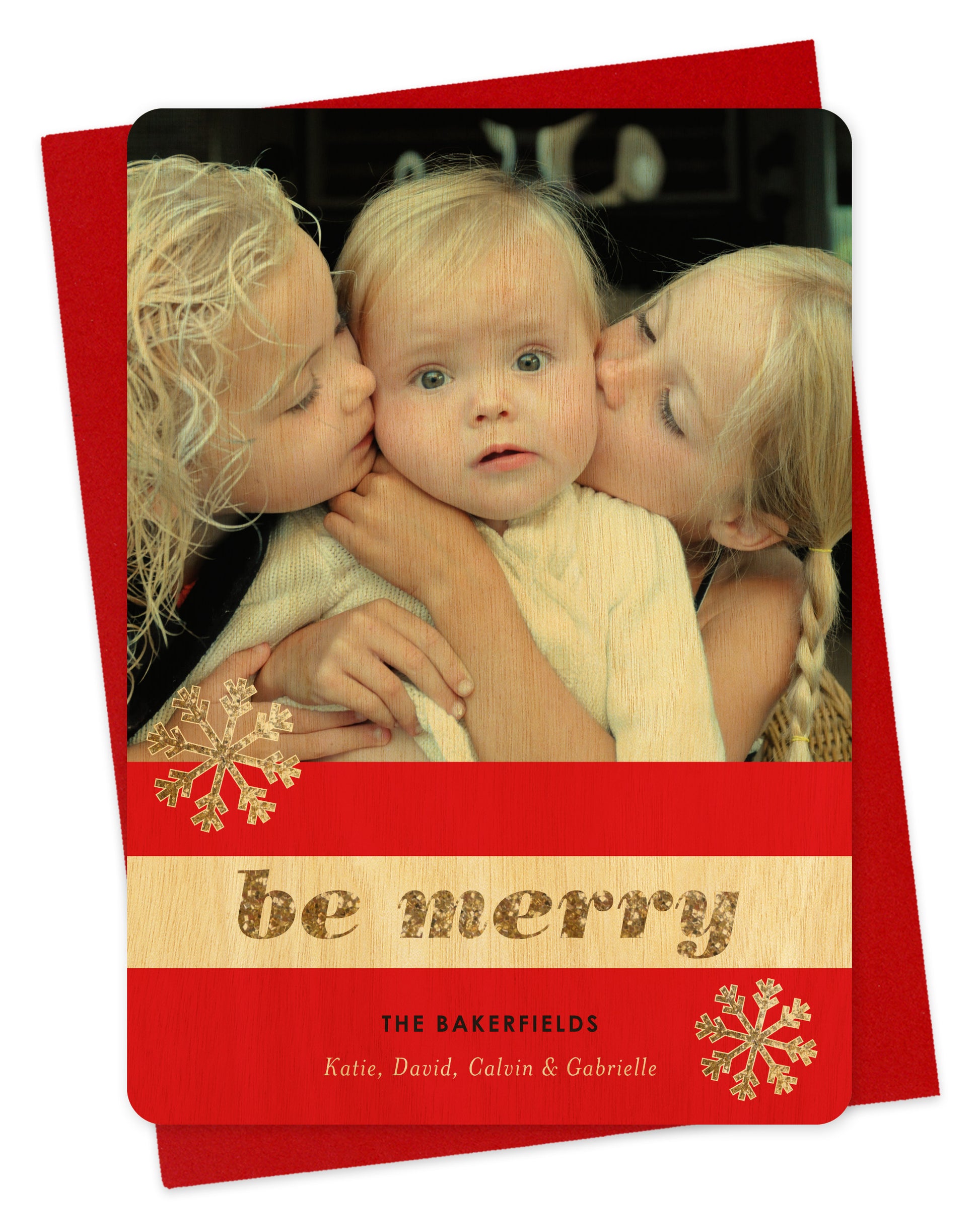 Customizable wood holiday card featuring a photo across the top, a red and birch wood striped banner with snowflakes and “Be Merry” in glittery gold font, plus a personal greeting. Shown with a red envelope.
