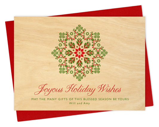 Customizable paper holiday card featuring a red and green snowflake on a printed birch wood grain background with a personal greeting. Shown with a red envelope.