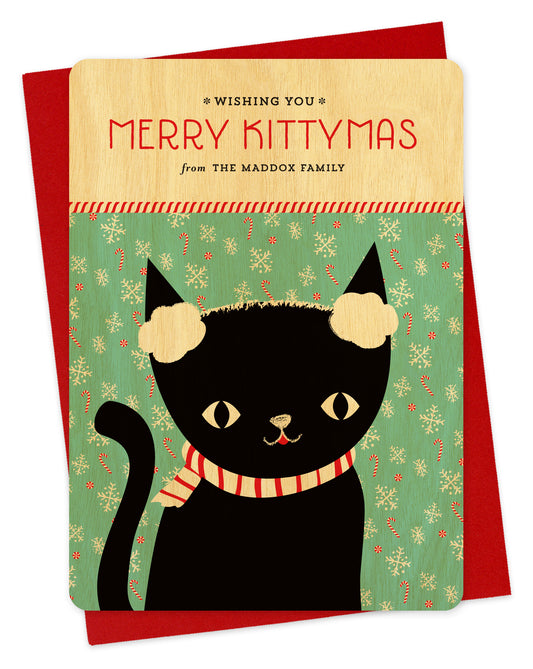 Customizable birch wood holiday card featuring a black cat wearing earmuffs in front of a festive backdrop, a "Merry Kittymas" sentiment and a personal greeting. Shown with a red envelope.