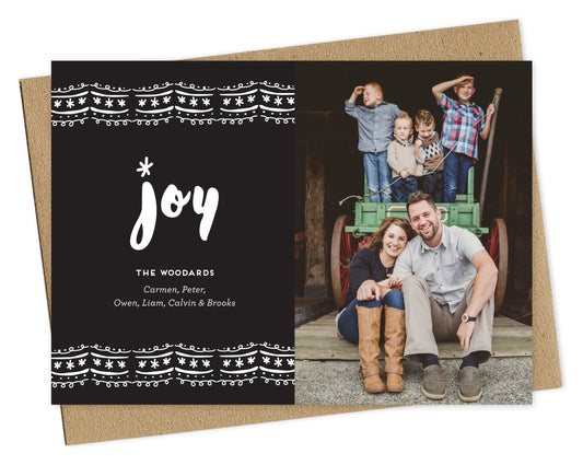 Customizable paper holiday card featuring a photo on the right and a bold black and white ric rac pattern with “joy” text and a personal greeting on the left. Shown with a kraft envelope.