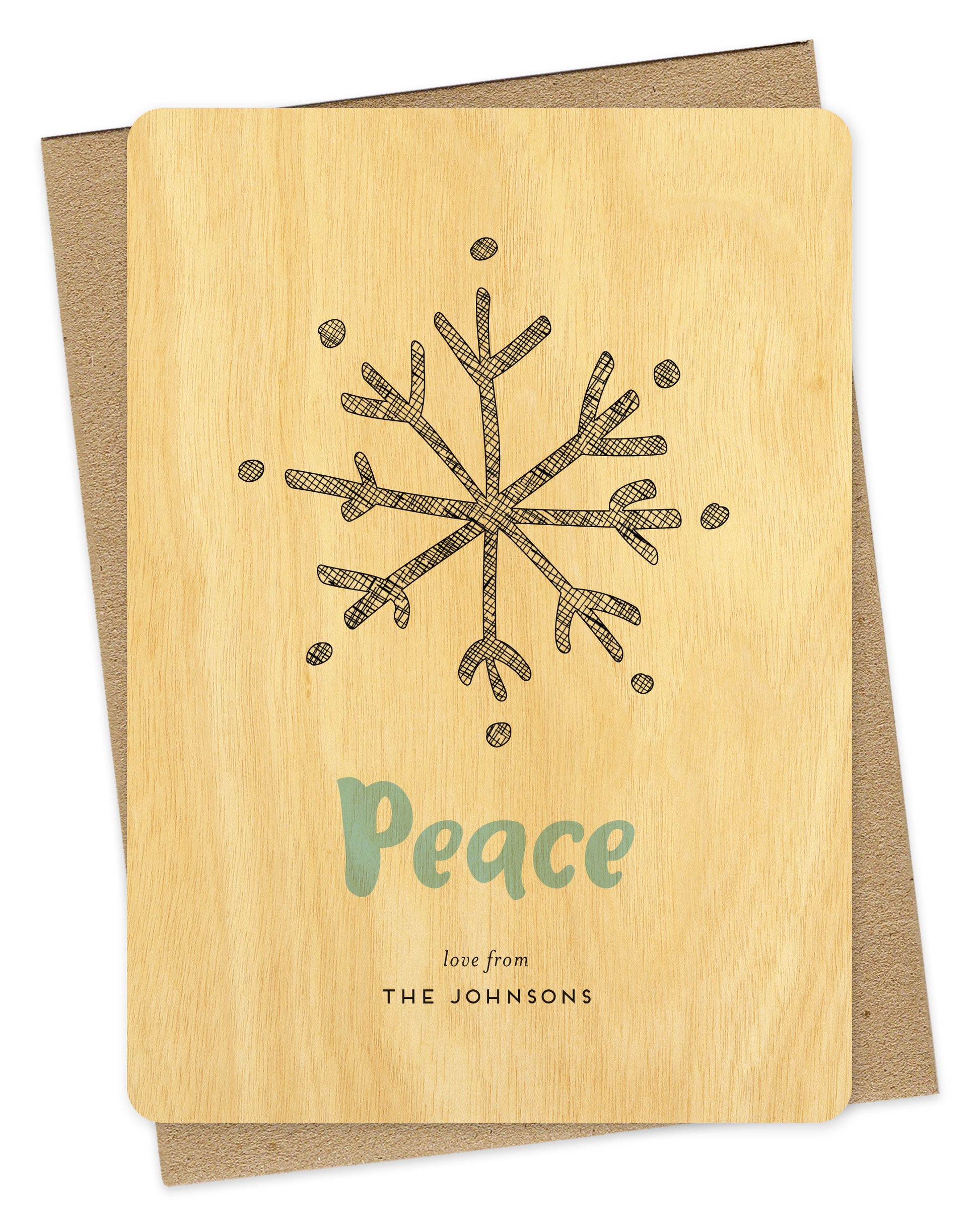Customizable wood holiday card featuring a large illustrated snowflake, aqua "Peace” text and a personal greeting against a birch wood backdrop. Shown with a kraft envelope.