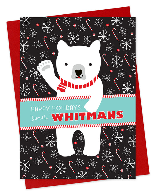 Customizable paper holiday card featuring a cheerful polar bear wearing a scarf and waving “Happy Holidays” against a black backdrop with candy canes and snowflakes. A banner across the middle displays a personal greeting. Shown with a red envelope.