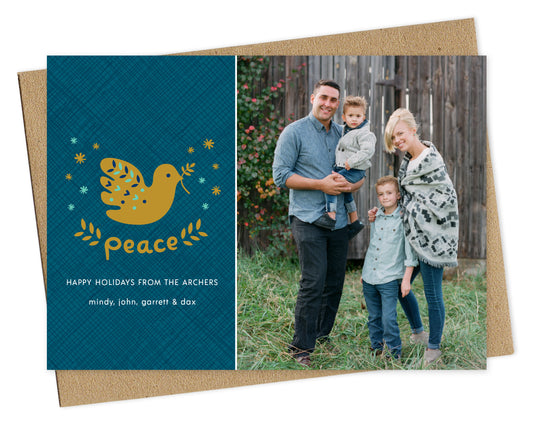 Customizable paper holiday card featuring a family photo on the right and a blue crosshatch pattern with “Peace” text, a dove carrying an olive branch and a personal greeting on the left. Shown with a kraft envelope.