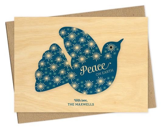 Customizable paper holiday card with blue dove, “Peace on Earth” sentiment, personal greeting and printed birch wood grain background. Shown with a kraft envelope.