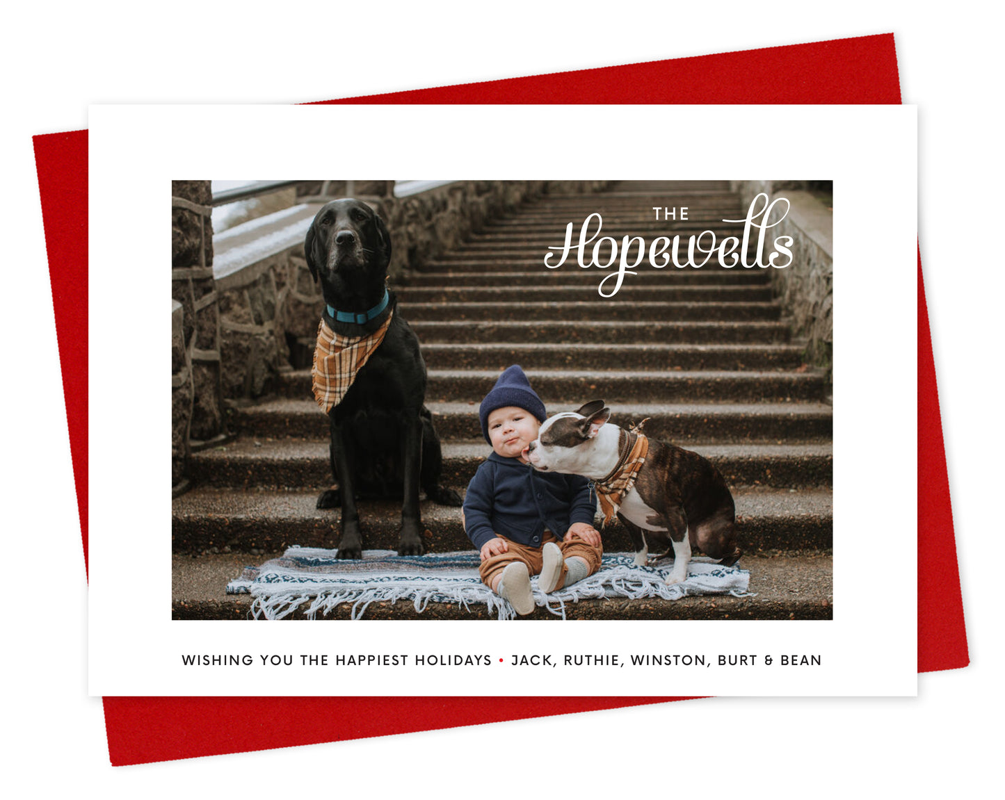 Customizable paper holiday card with a photo framed by a white border, a family name in knockout style over the photo and a personal greeting on the bottom. Shown with a red envelope.